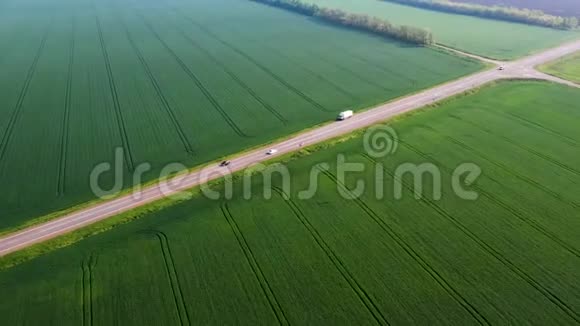 一辆白色汽车在公路上的绿色田野之间的移动麦田视频的预览图