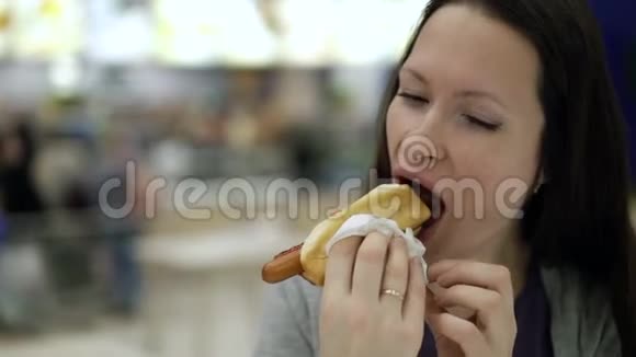 年轻漂亮的女人在快餐店吃美味的热狗在食物场咀嚼食物的饥饿妇女视频的预览图