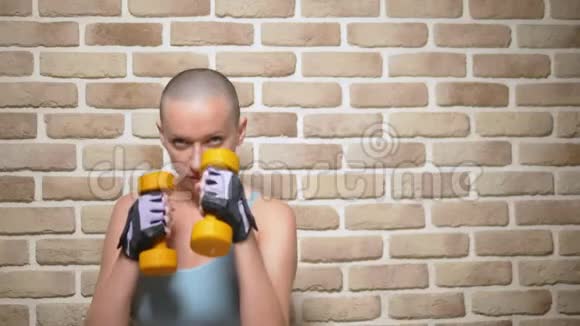 秃头的女人正在镜头前拳击手里拿着哑铃在砖墙的背景上复制空间视频的预览图