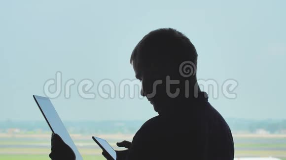 年轻人在飞机起飞的背景下使用平板电脑和手机的剪影视频的预览图
