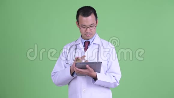 快乐的亚洲男子医生思考使用数码平板电脑视频的预览图