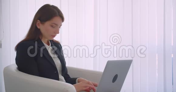 一位年轻成功的女商人用笔记本电脑看着相机开心地坐着微笑的特写侧景视频的预览图
