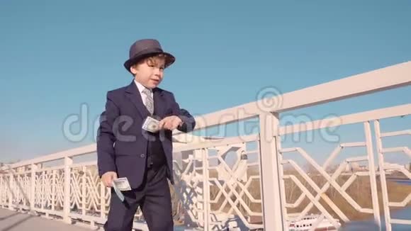 穿着黑色西装戴帽子从桥上扔钱的小商人浪费金钱视频的预览图