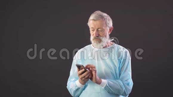 旧外科医生的画像老外科医生在黑暗的背景下使用智能手机视频的预览图