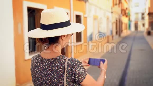 西班牙阿利坎特的一条狭窄的Denia街上一位带着稻草遮阳帽的旅游妇女拍照视频的预览图