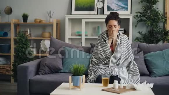 生病的年轻女子咳嗽坐在家里的沙发上喝药视频的预览图