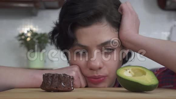 饥饿的美丽女孩的特写肖像在美味的巧克力蛋糕和美味的糖霜之间选择视频的预览图
