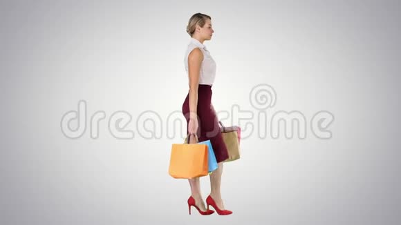 快乐全长的女人每只手都拿着纸购物袋在梯度背景下行走视频的预览图