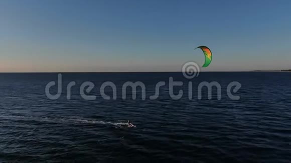 一个人带着他的绿色风筝在海里风筝在他身后带着夕阳冲浪视频的预览图