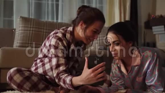 两个姐妹双胞胎在智能手机上看着有趣的东西在舒适的客厅里笑着视频的预览图