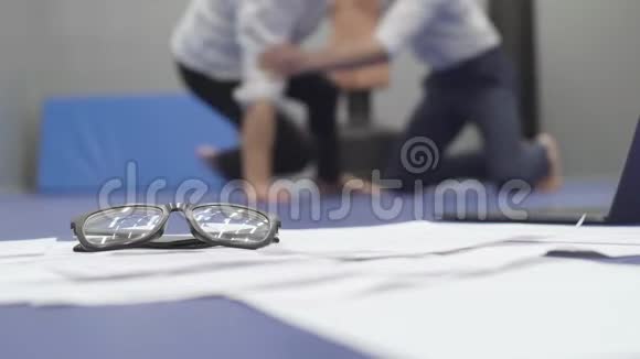 两个穿着白色衬衫的男人在背景中摔跤和握把躺在地板上的模糊身影文件视频的预览图