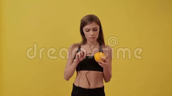 运动女孩连接耳机到橙色和听音乐工作室黄色背景视频的预览图