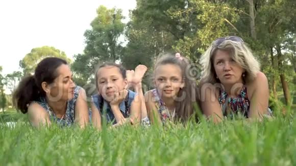 日落时分两位母亲和两个小女儿躺在公园的绿草上玩耍和亲吻肖像关闭视频的预览图