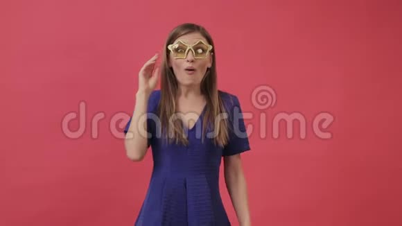 美丽的女孩穿着一件连衣裙戴着黄色的眼镜以星星的形式跳舞紫色背景工作室视频的预览图