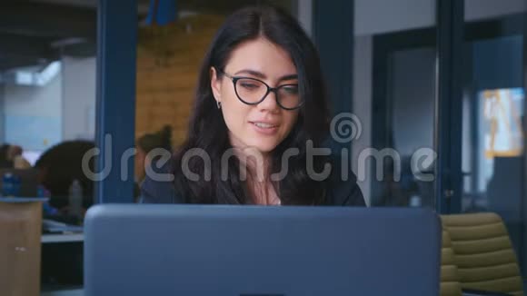 商务女性感到快乐微笑着看着办公室的镜头年轻女性在办公桌上使用笔记本电脑视频的预览图