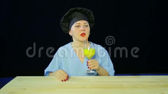 一位黑色背景下的女厨师品尝水果奶昔并展示班的签名视频的预览图