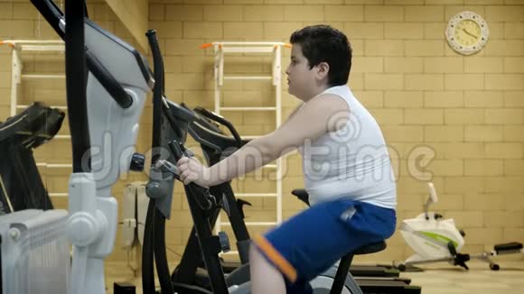 肥胖的小男孩在健身房锻炼自行车健康生活方式视频的预览图