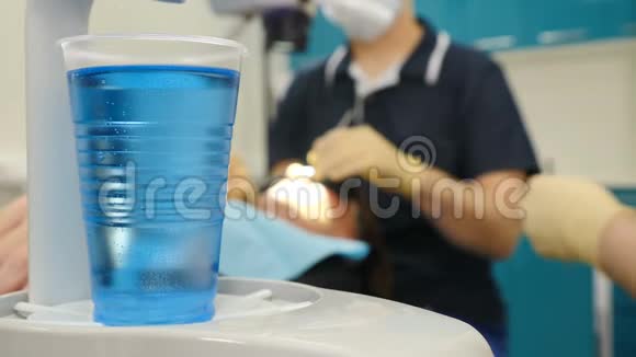 在第一个计划中用蓝色液体拍摄塑料玻璃片并模糊牙医和助理制作牙科手术视频的预览图