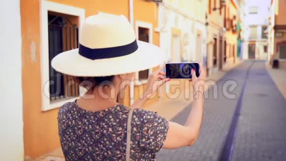 西班牙阿利坎特的一条狭窄的Denia街上一位带着稻草遮阳帽的旅游妇女拍照视频的预览图