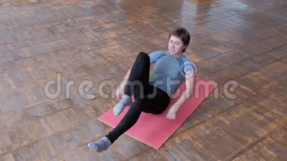 运动女孩躺在粉红色的垫子上做一套健身运动以加强腹部肌肉身体反射带t的房间视频的预览图