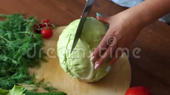 一个女人的特写把一把刀切在一个切割板上的半白菜上视频的预览图