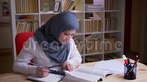 穆斯林成年女学生戴头巾参加医学考试阅读一本书并在书中做笔记的特写镜头视频的预览图