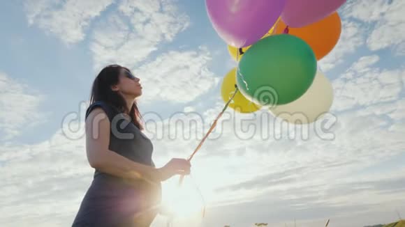 在蓝天背景下一位无忧无虑的孕妇在草地上玩气球视频的预览图