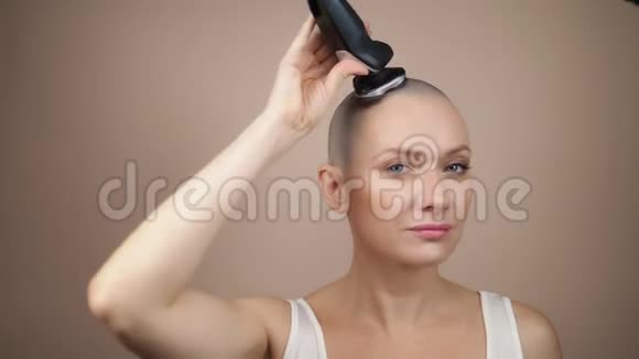 一个年轻迷人的秃头女孩用电动剃须刀剃光头米色背景视频的预览图