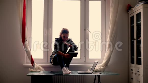 年轻的女人坐在家里的窗户上有一台在线平板电脑家庭内部2025岁视频的预览图
