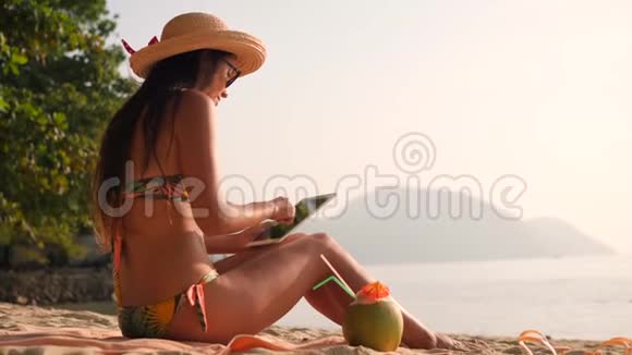 比基尼的年轻旅游妇女使用移动平板小玩意坐在热带天堂桑迪海滩4K慢动作视频的预览图