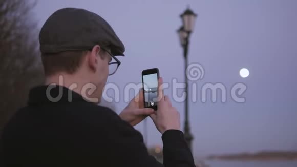 日落时分一个年轻人站在河边风景如画的地方借助智能手机欣赏风景视频的预览图