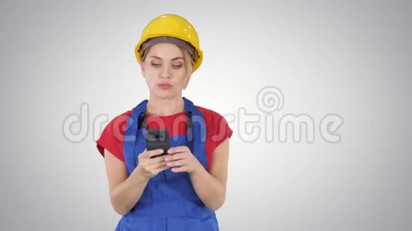 年轻的职业女性承包商穿着硬帽子短信与手机梯度背景视频的预览图