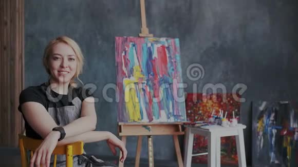 灵感来自美丽的金发女艺术家坐在她的工作场所她微笑着看着镜头现代视频的预览图
