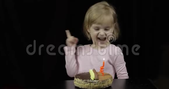 小可爱的女孩在黑色背景的生日蛋糕上吹上节日的蜡烛视频的预览图