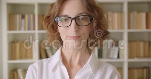 戴着眼镜的白种人成年女商人的特写照片看着镜头在室内愉快地微笑着视频的预览图