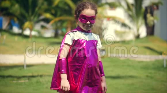 美丽的小女孩在超级英雄服装穿着斗篷和面具的英雄看着镜头一种概念视频的预览图
