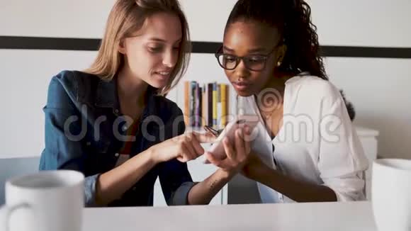 两个年轻漂亮的商务女性在办公室休息时一起使用手机视频的预览图