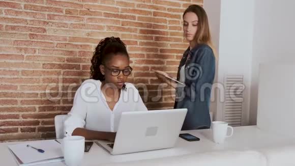 两位年轻漂亮的商务女性在办公室里和数码平板电脑和笔记本电脑一起工作视频的预览图