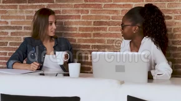 两个年轻漂亮的商务女性在办公室休息时一边聊天一边喝咖啡视频的预览图