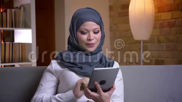 使用平板电脑拍摄穆斯林成年女性戴头巾的特写镜头坐在沙发上显示绿色屏幕视频的预览图
