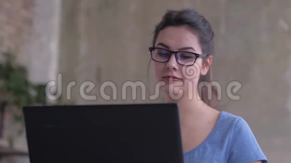 在家庭教育特写中戴眼镜的现代女孩看着笔记本电脑屏幕在键盘上输入文字视频的预览图