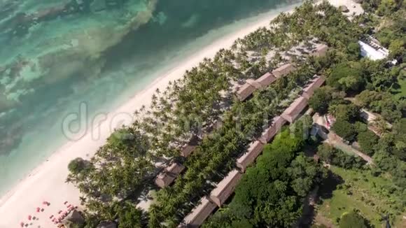 在沙滩上的海浪绿棕榈树酒店房屋和度假胜地的无人机拍摄视频的预览图
