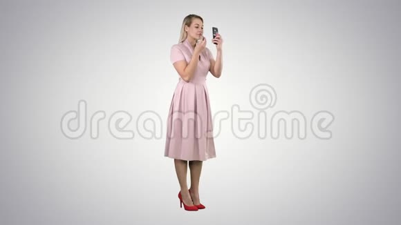 涂口红的女人在渐变背景下看着她的手机视频的预览图