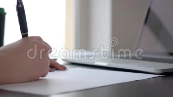 在笔记本电脑背景特写的工作桌上用钢笔书写女性手写文件视频的预览图