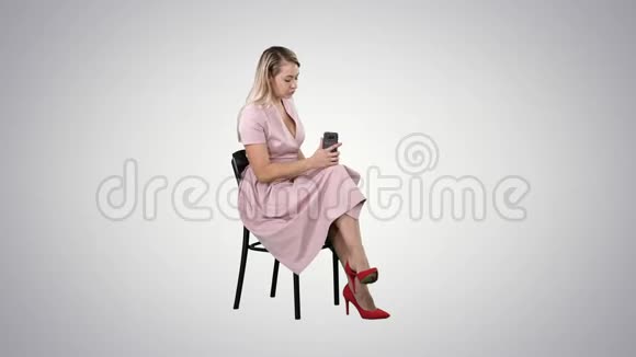 年轻的女人金发坐在椅子上看书在渐变背景下用手机发短信视频的预览图