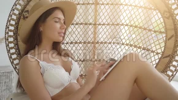网上购物性感女人坐在舒适的扶手椅里一边拿着银行卡一边通过平板电脑上网购物视频的预览图