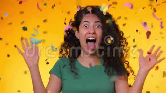 年轻的拉丁女孩卷发跳舞在黄色背景下的纸屑雨中玩得很开心女人庆祝视频的预览图
