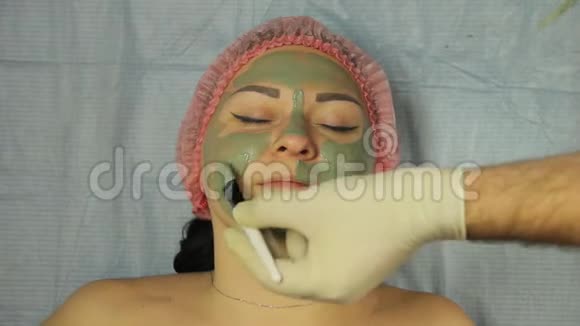 一位戴手套的男性美容师用特殊的刷子在客户的脸上涂上一层泥视频的预览图