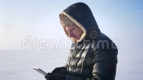 穿着外套和引擎盖的商人站在冰冻的湖面上认真地展示了平板电脑的绿色屏幕以推荐应用程序视频的预览图