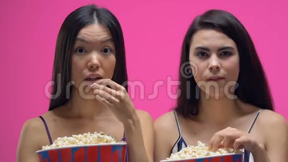 两个穿着睡衣的女人吃着爆米花聚精会神地看着有趣的电影视频的预览图